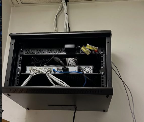 Open wall-mounted cabinet holding network equipment and cabling
